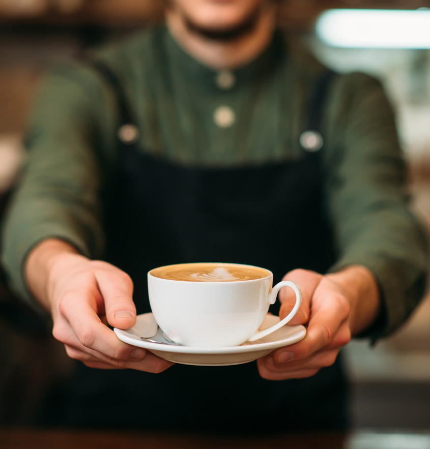 Ein Mann hält eine Tasse Cappuccino in die Kamera