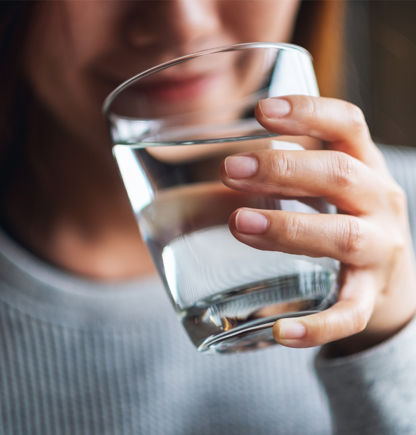 Eine lächelnde Frau führt ein Glas an ihren Mund, um Wasser daraus zu trinken