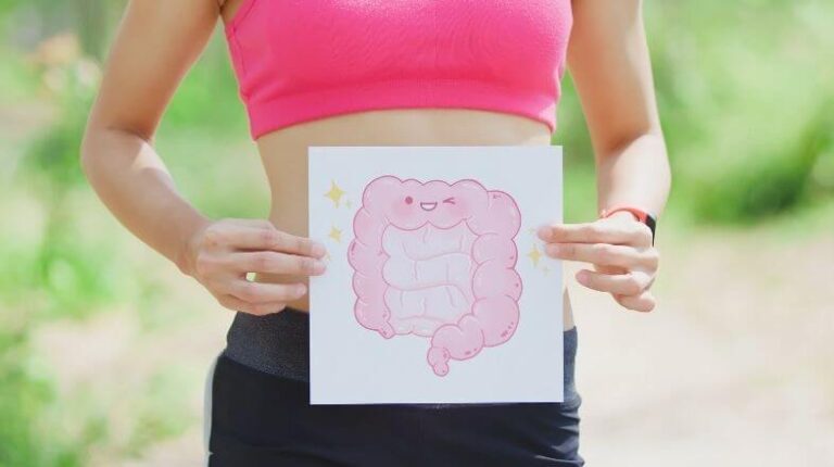 Eine sportliche Frau hält ein Bild eines lächelnden Darmtraktes vor ihren Bauch. Damit soll Darmgesundheit symbolisiert werden