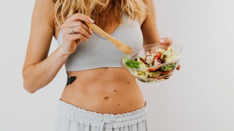 Eine sportliche Frau hält eine Schüssel Salat in der Hand und symbolisiert somit gesunde Ernährung